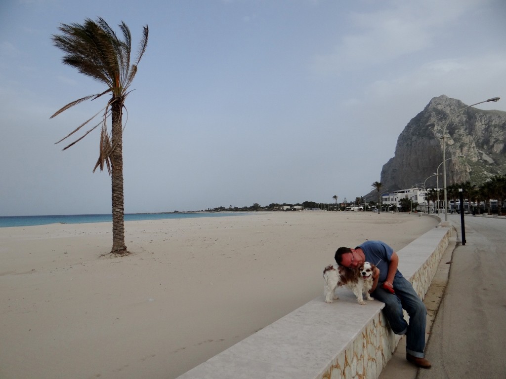 Jay naps on Charlie by San Vito beach, still windy and a Gibraltarian style rock looming over it.