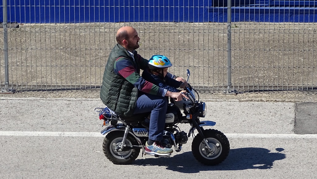 Man and child on monkey bike at racing circuit.