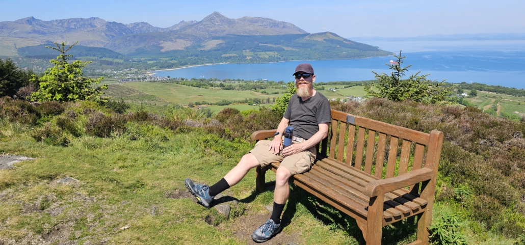 Jay on a bench with a view of Brodick bay behind him