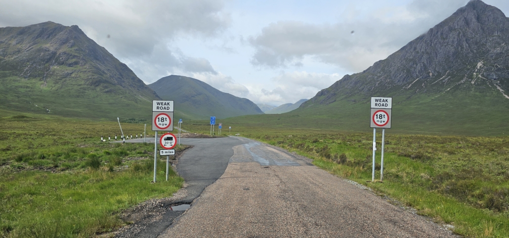 Single track road with 18 tonne weight limit signs at entrance and green mountains behind
