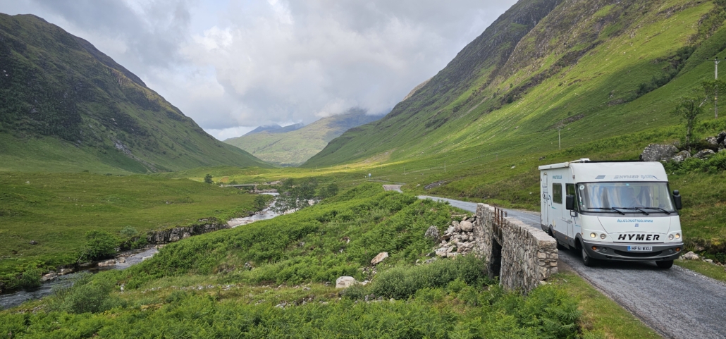 Motorhome driving up valley road with mountains either side