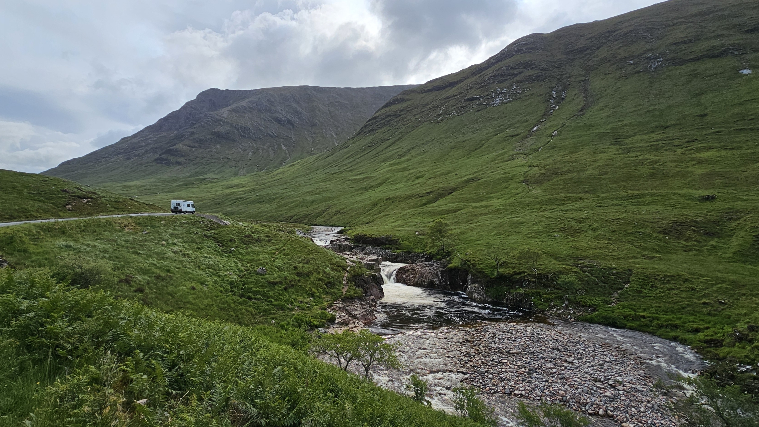 Motorhome parked overlooking stream running down valley between green mountains